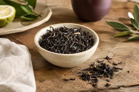 Feuilles de thé noir Earl Grey en vrac près d’une tasse ambrée, sur une table en bois patiné