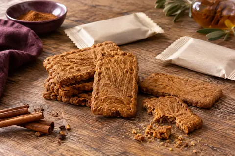 Biscuits speculoos caramélisés et sachets individuels présentés avec une tasse de café sur une table en bois.