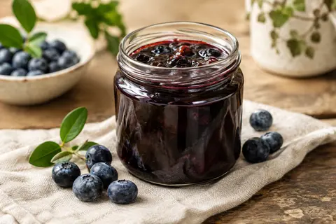 Pot de confiture de myrtille avec morceaux, accompagné de quelques myrtilles fraîches sur une table en bois