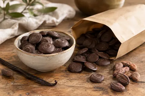 Callets de chocolat noir de couverture dans un bol, avec un sachet neutre sur une table en bois.