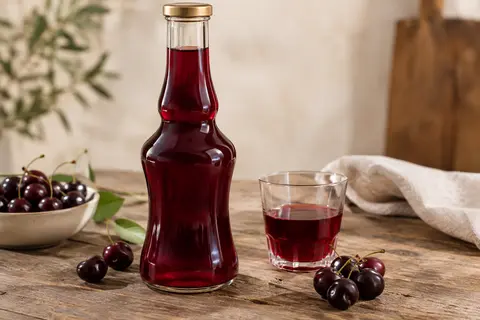 Flacon de sirop de cerise Amarena posé sur une table en bois, avec quelques cerises et un verre.