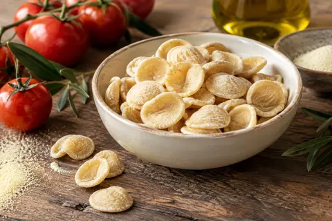 Orecchiette sèches en semoule de blé dur dans une assiette crème sur une table en bois patiné.
