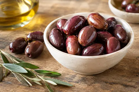 Olives Kalamata brun rougeâtre avec noyau, servies dans un bol sur une table en bois.