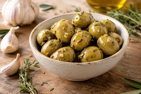 Olives vertes Manzanilla à l’ail et aux herbes servies dans un petit plat sur une table en bois