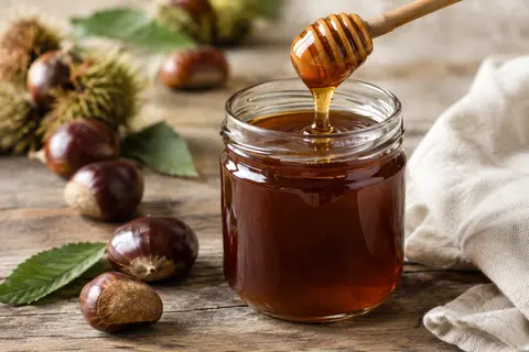 Pot de miel de châtaignier foncé accompagné d’une cuillère et de châtaignes
