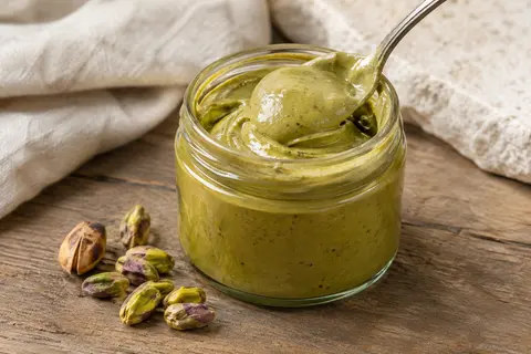 Crème de pistache onctueuse dans un bol, accompagnée de quelques pistaches sur une table en bois
