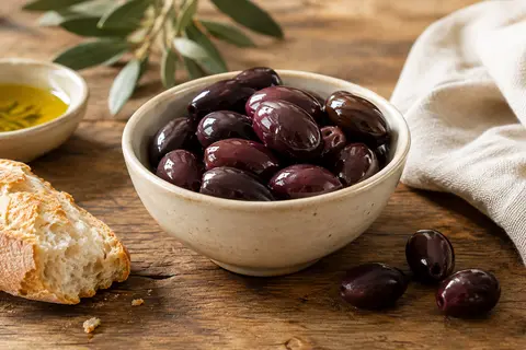 Olives Kalamata grecques brun foncé dans un plat en céramique crème sur une table en bois patiné.