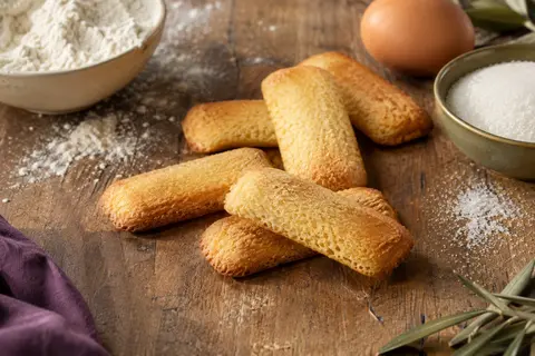 Biscuits Pavesini dorés et plats disposés sur une assiette claire, avec une tasse de café en arrière-plan
