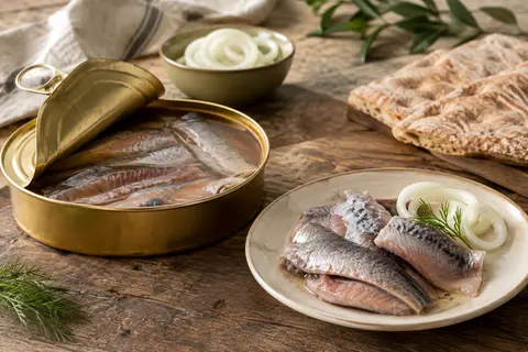 Boîte de surströmming ouverte avec des filets de hareng sur une table en bois, accompagnée de pain et de pommes de terre.