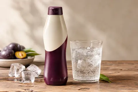 Flacon de concentré Pepsi Zero Sucres posé près d’un verre d’eau pétillante sur une table en bois.