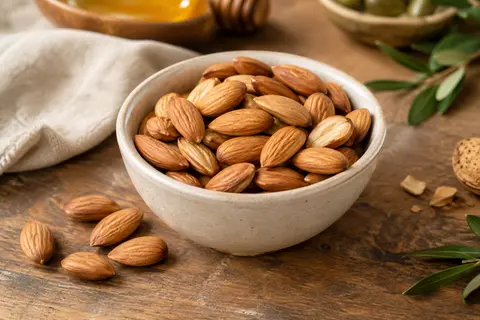 Amandes décortiquées entières dans un bol crème, posées sur une table en bois patiné.