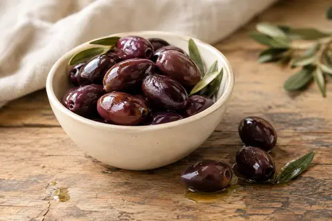 Olives noires Kalamata à l’huile d’olive servies dans un bol sur une table en bois patiné.