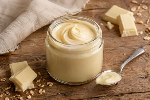 Pot de pâte à tartiner au chocolat blanc avec une portion servie sur une cuillère, sur une table en bois